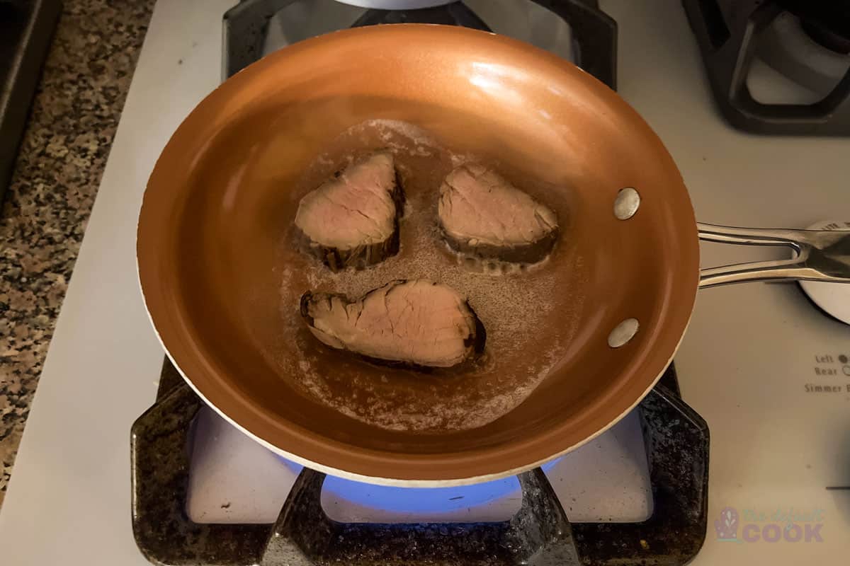 Three slices of pork tenderloin and a bit of butter in a small skillet with the flame on.