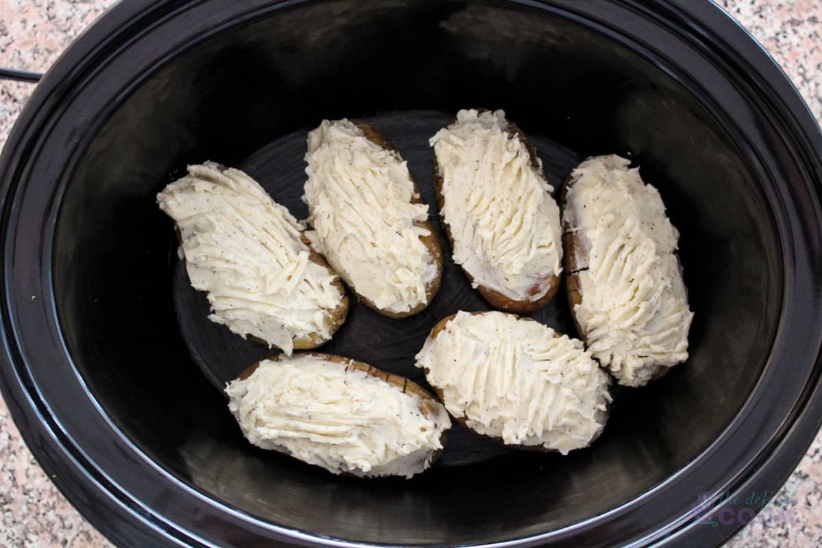 6 prepared potatoes in an oval slow cooker ready to turn on.
