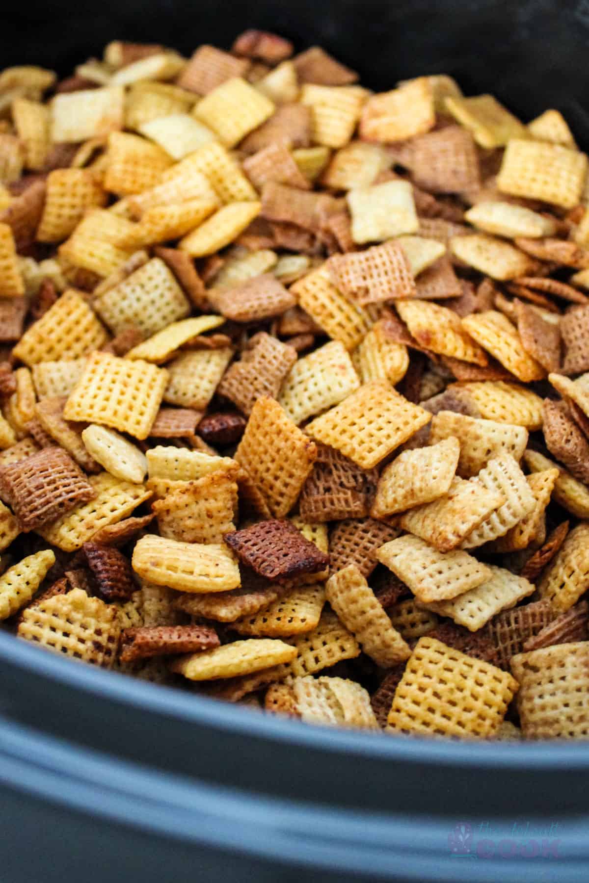 Close up of a slow cooker filled with seasoned chex.