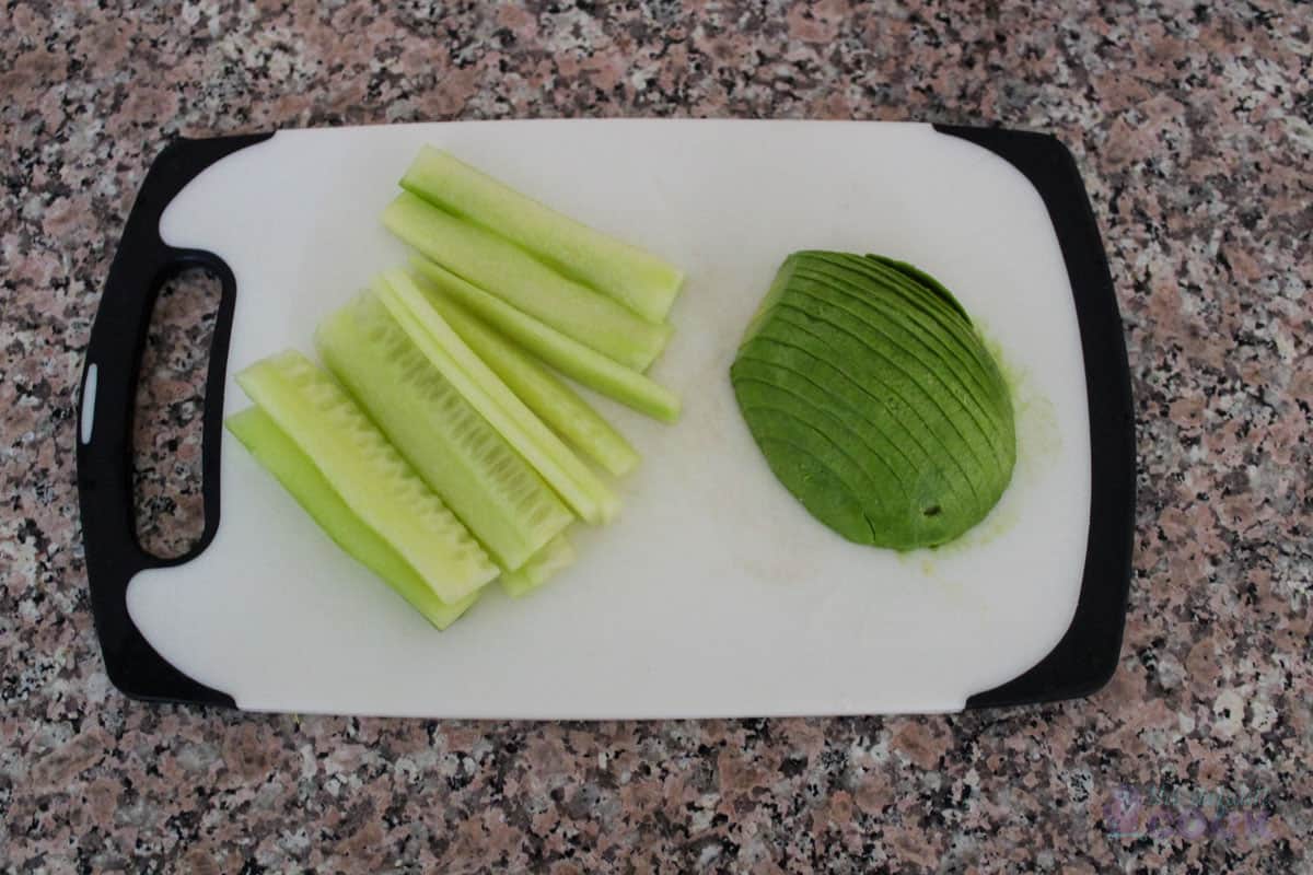 Cut sticks of cucumber and slices of avocado on a cutting board.