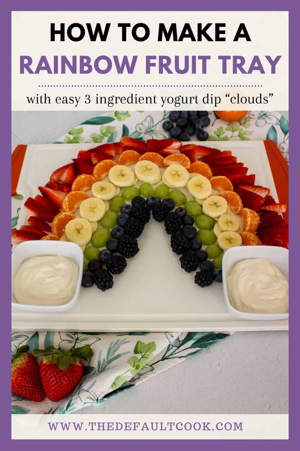 A fruit platter arranged in a rainbow pattern on a white serving tray, with yogurt dips on either side, against a white tile background with a decorative napkin, and text above reading "how to make a rainbow fruit tray with easy 3 ingredient yogurt dip clouds" and the website name below. 