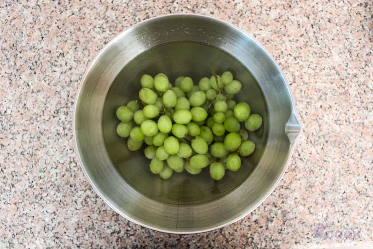 A bowl sitting on a kitchen counter filled with green grapes covered with water and vinegar.