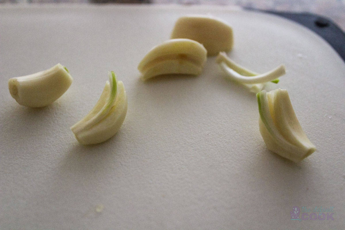 Close up of garlic cloves cut in half with green centers, some of which have been removed.