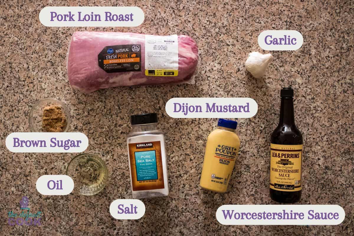 Ingredients on a kitchen counter with labels added by each ingredient: pork loin roast, garlic, brown sugar, oil, salt, dijon mustard, and worchestershire sauce.