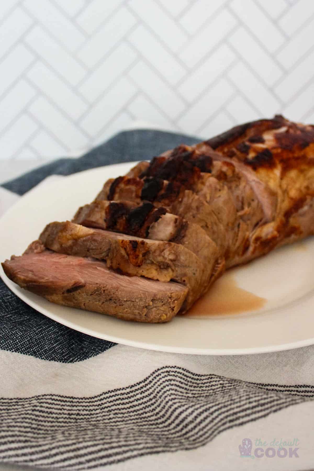 Sliced pork loin roast on a white serving plate on a blue and white kitchen towel, with a clear view of the tender, pink center and crispy, charred exterior.