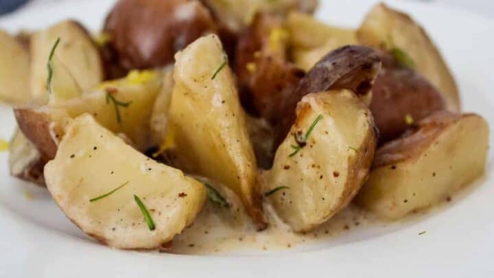 Potatoes in a light cream sauce with fresh dill on a white plate on a blue and white kitchen towel.