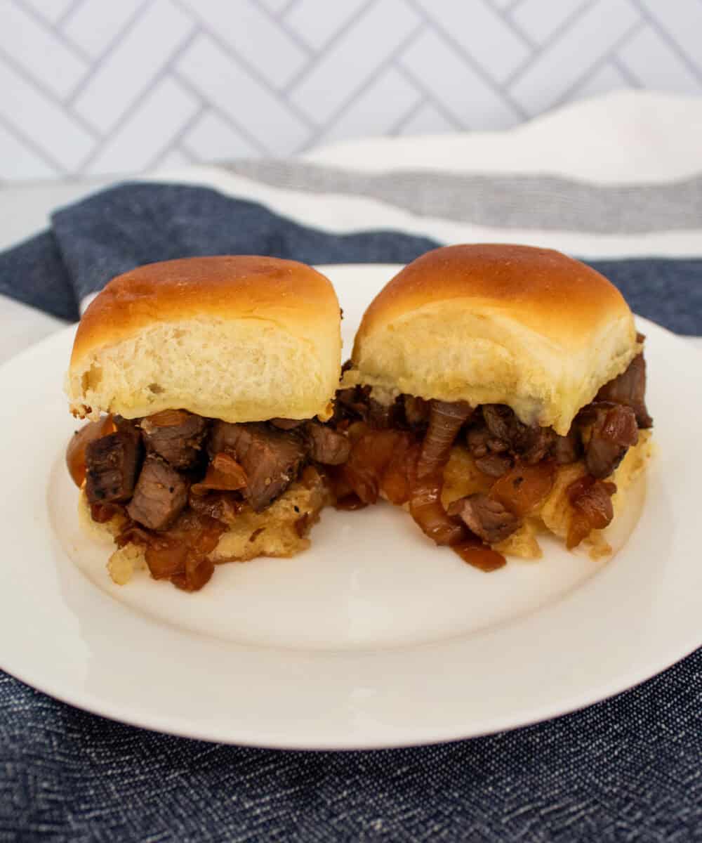 Two tri tip sliders on a white plate on a blue and white kitchen towel.