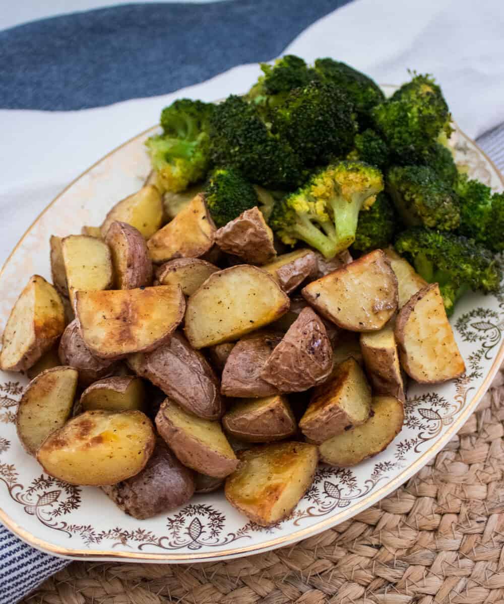 A decorative plate filled with roasted potato wedges and broccoli, placed on a woven placemat beside a blue and white striped cloth.