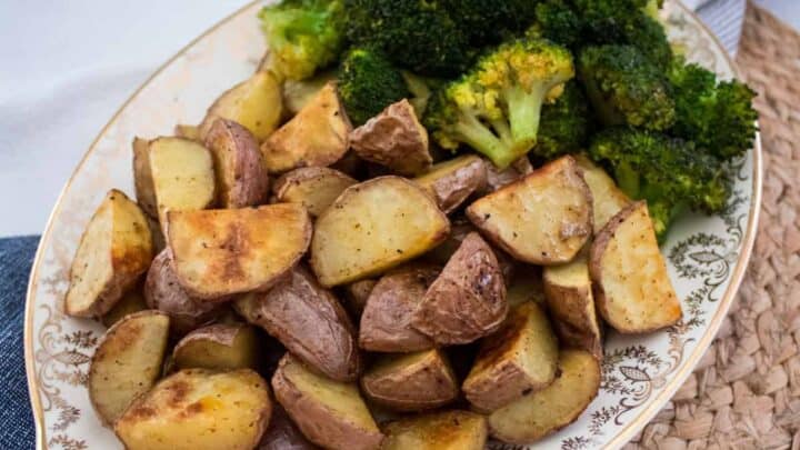 A decorative plate filled with roasted potato wedges and broccoli, placed on a woven placemat beside a blue and white striped cloth.