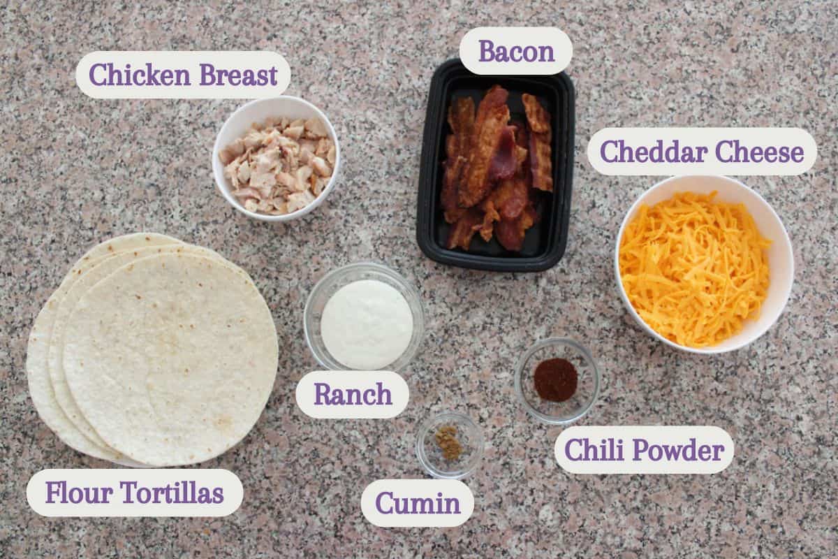 A countertop displays labeled ingredients: a bowl of chopped chicken breast, cooked bacon strips, shredded cheddar cheese, flour tortillas, ranch dressing, cumin, and chili powder.