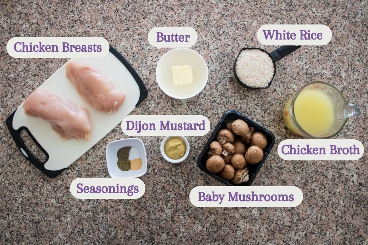 Top-down view of labeled ingredients on a countertop: chicken breasts, white rice, butter, Dijon mustard, baby mushrooms, chicken broth in a measuring cup, and seasonings in small bowls.