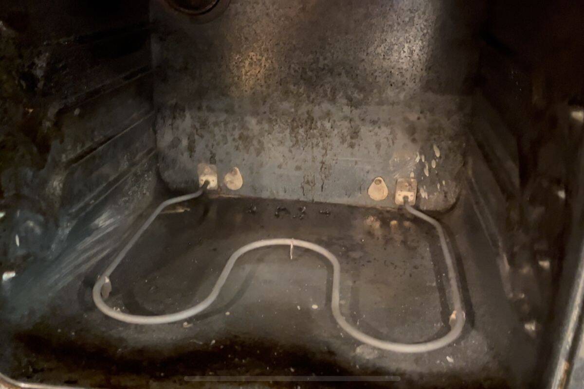 View of the inside of an oven, showing the metal heating element at the bottom and visible grime and stains.