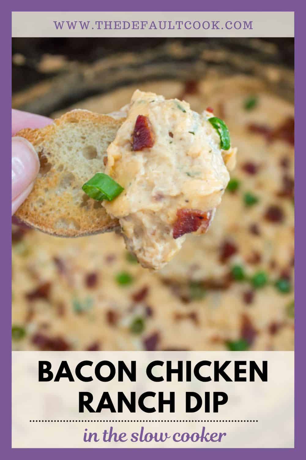 A hand holds a toasted bread slice topped with creamy bacon chicken ranch dip, garnished with bacon bits and green onions. The dip and more garnish are visible in a blurred background slow cooker dish.