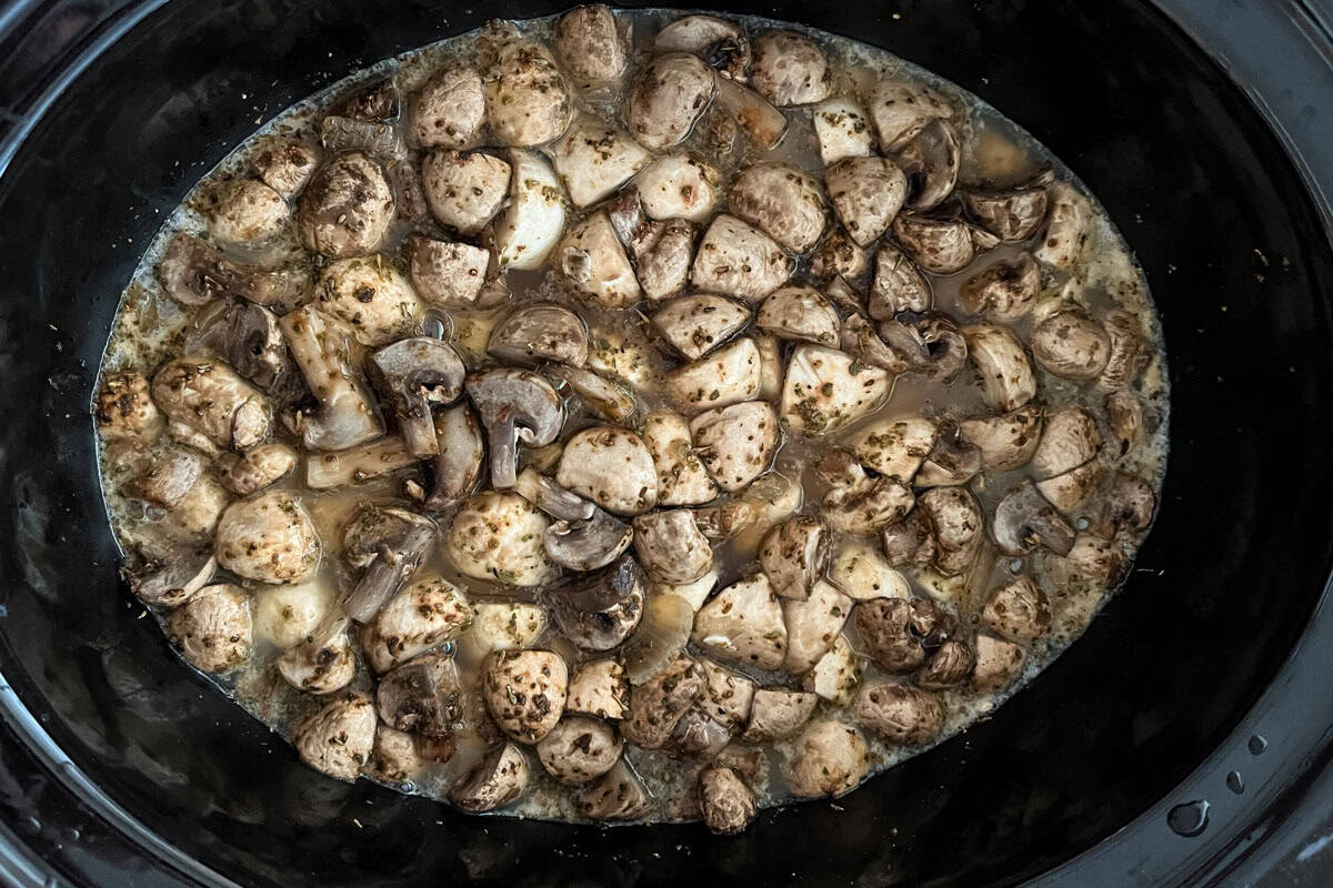 Chopped mushrooms cooking in a slow cooker, surrounded by a seasoned broth or sauce, creating a hearty and savory mixture.