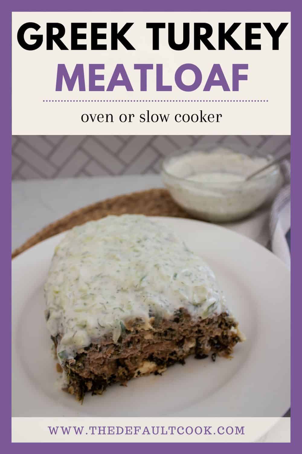 A slice of Greek turkey meatloaf topped with a creamy white sauce sits on a white plate. In the background, there’s a bowl of the same sauce. Text reads: “Greek Turkey Meatloaf, oven or slow cooker, thedefaultcook.com.”.