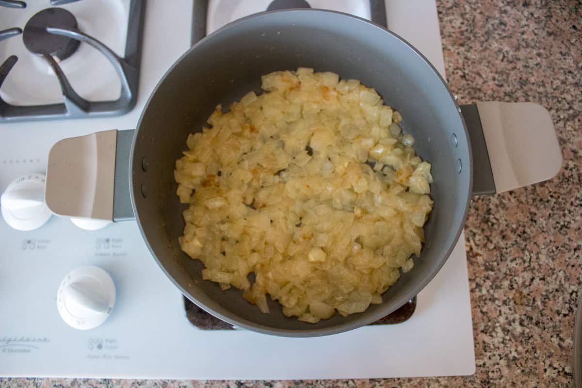 A pot of chopped onions sautéing on a stovetop, with the onions turning translucent and slightly golden. The stove and granite countertop are visible in the background.