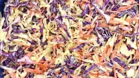 A blue bowl filled with coleslaw made of shredded green cabbage, purple cabbage, and carrots, mixed with a creamy dressing and sprinkled with black pepper.