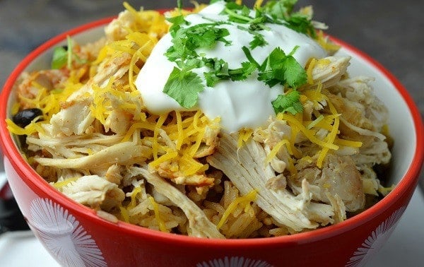 A bowl of shredded chicken, rice, shredded cheese, black beans, topped with a dollop of sour cream and chopped cilantro.