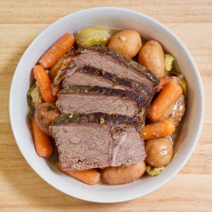 Sliced pot roast served in a white bowl with baby potatoes and whole carrots.