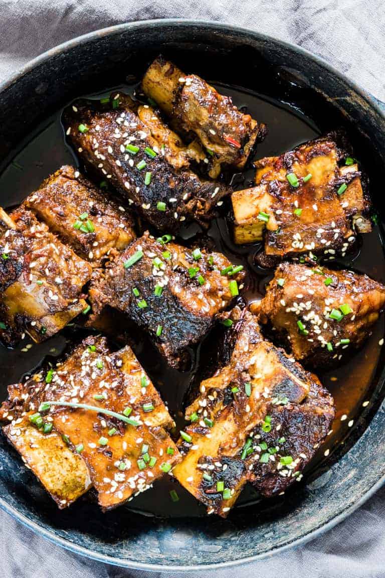 Braised short ribs topped with sesame seeds and chopped chives in a dark sauce.