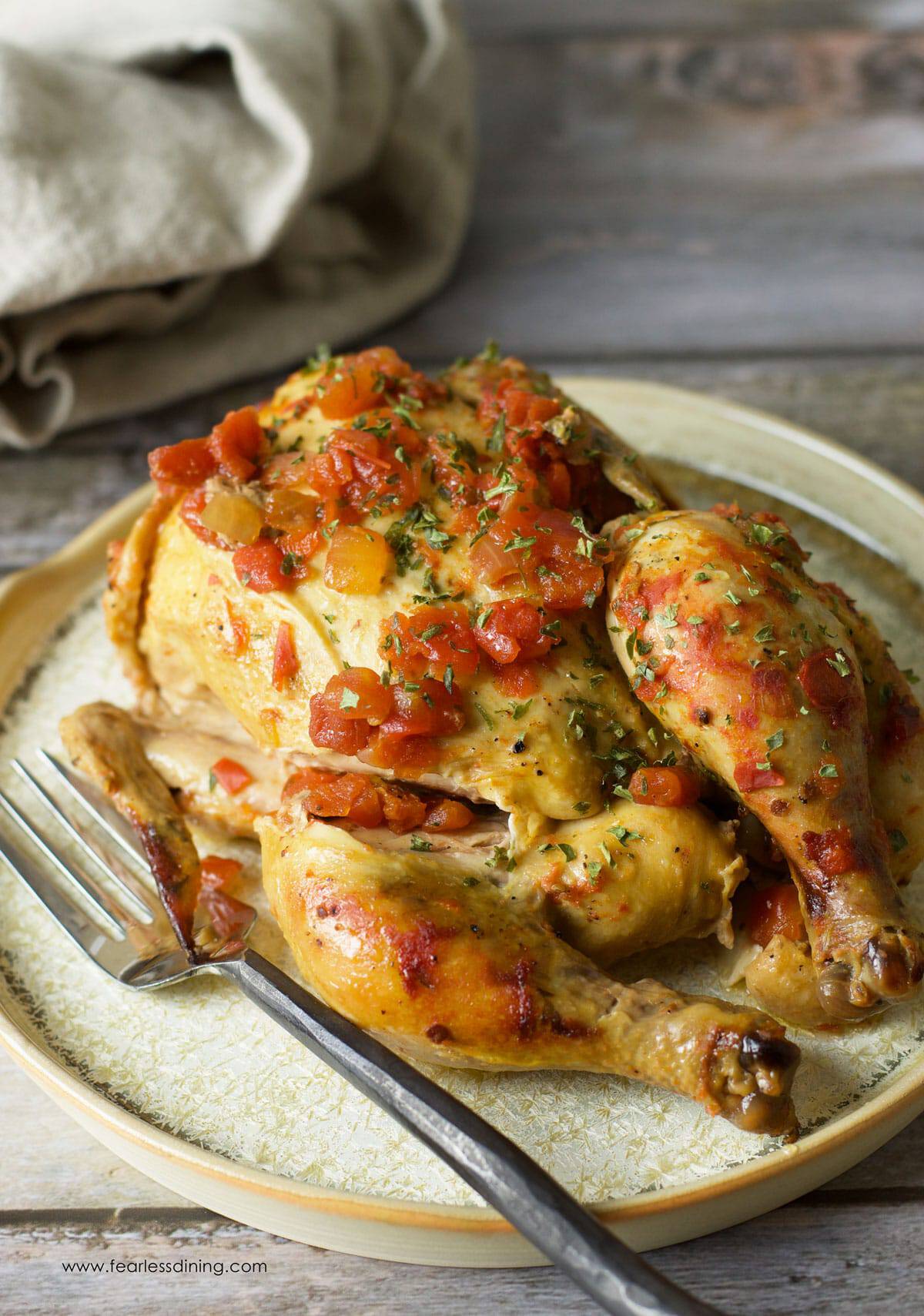 Roasted chicken topped with diced tomatoes and herbs on a decorative plate with a fork.