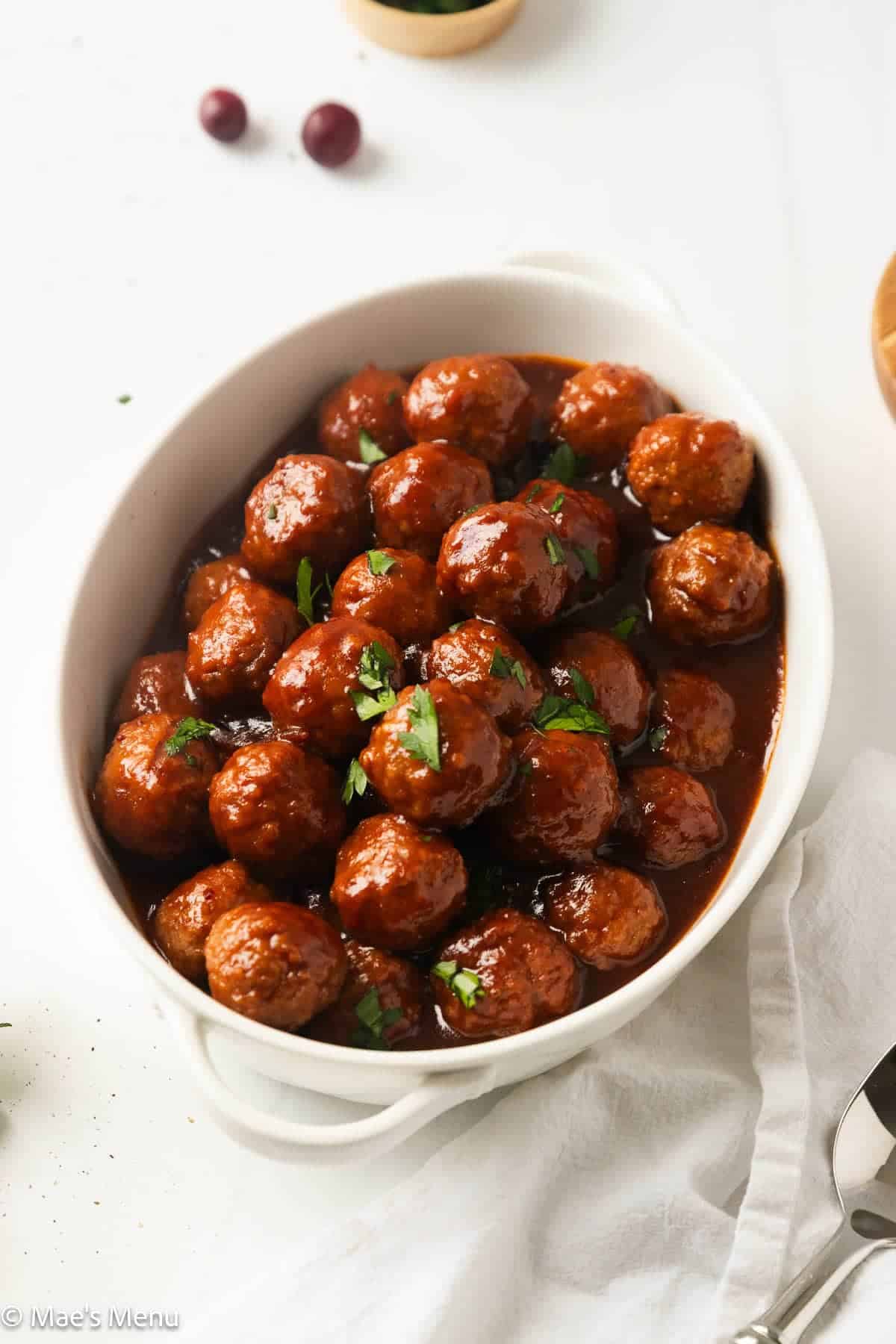 A white oval serving dish filled with meatballs in a dark glaze, garnished with fresh parsley.