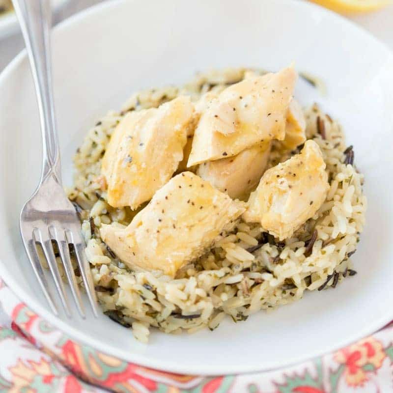 A white bowl with seasoned chicken pieces on top of a bed of wild rice, with a fork resting on the side of the dish.