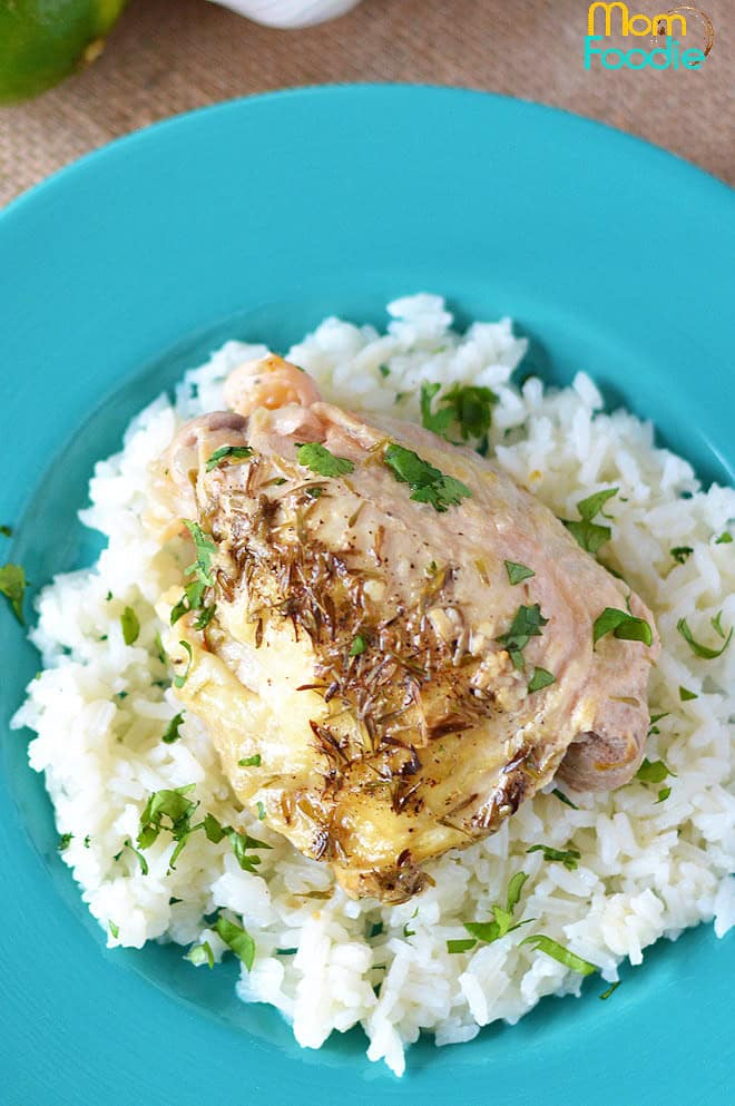 Cooked chicken with herbs served on a bed of white rice, garnished with chopped parsley, on a turquoise plate.