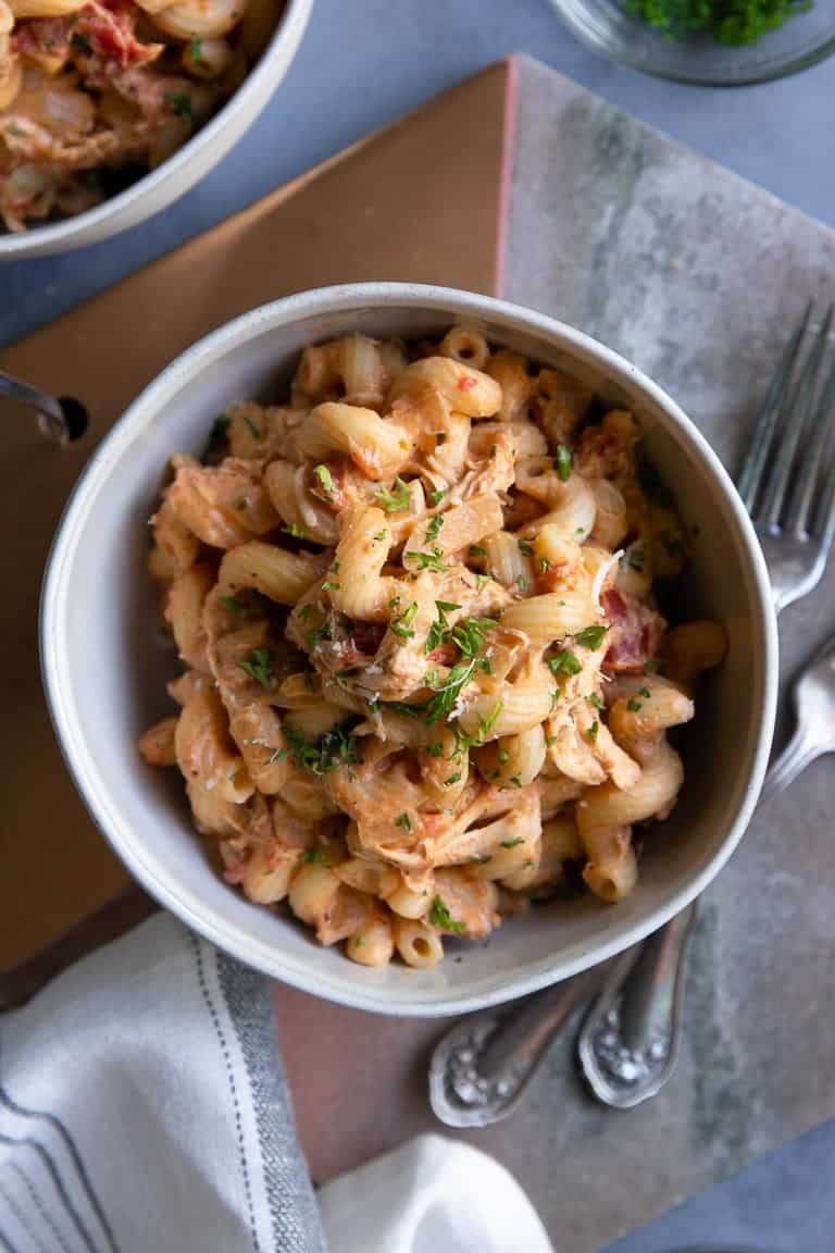 A bowl of creamy tomato pasta with shredded chicken, garnished with fresh herbs.